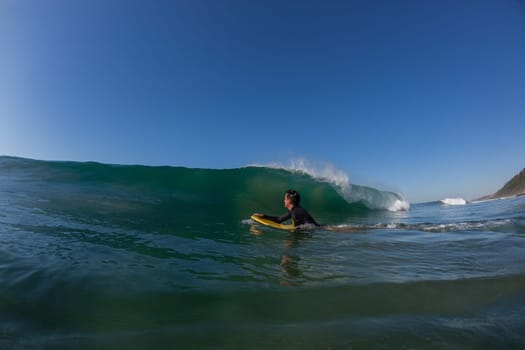 Ocean wave crashing on shallow reef with body-boarder paddling out to catch next surfing wave.