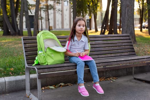Thoughtful young girl with backpack resting on park bench in autumn setting.