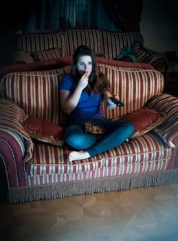 Beautiful brunette woman watching TV at night on sofa and eating popcorn