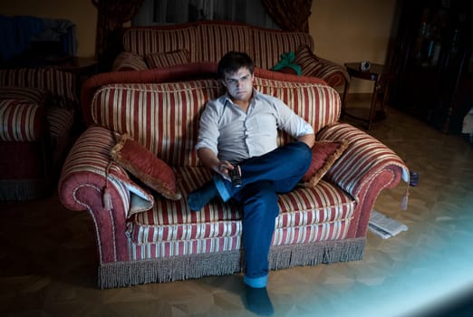 Portrait of man switching TV channels while sitting on sofa