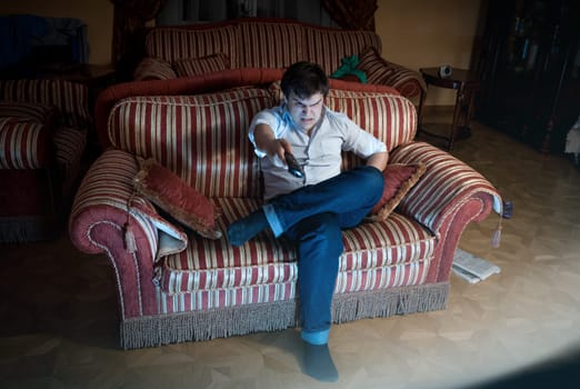 Portrait of angry man switching TV channel while sitting on sofa