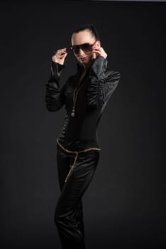 Portrait of beautiful Caucasian woman putting on sunglasses and wearing black bodysuit against black background