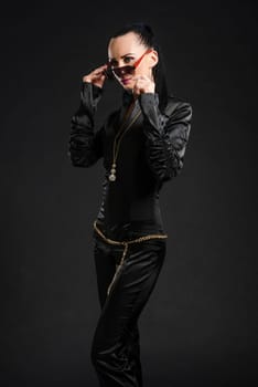 Portrait of beautiful Caucasian woman putting on sunglasses and wearing black bodysuit against black background