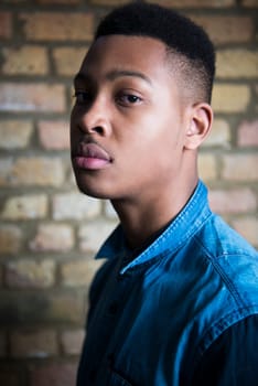 Shallow depth of field portrait of handsome dark skinned male model wearing casual clothes against brick wall