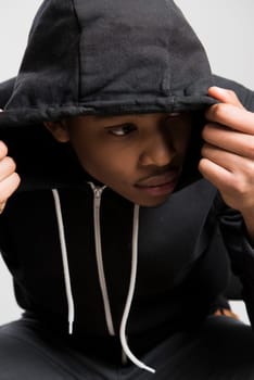 Portrait of suspicious dark skinned male model hiding under black hooded jumper
