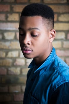 Shallow depth of field portrait of handsome dark skinned male model looking down and wearing casual clothes against brick wall