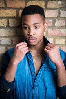 Portrait of handsome dark skinned male model wearing casual clothes against brick wall