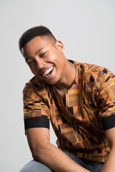 Portrait of handsome dark skinned male model smiling and wearing traditionally African clothes against white background
