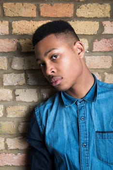 Portrait of handsome dark skinned male model wearing casual clothes against brick wall