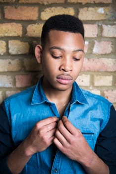 Portrait of handsome dark skinned male model wearing casual clothes against brick wall