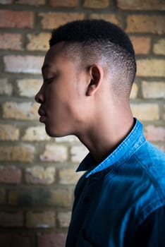 Shallow depth of field profile portrait of handsome dark skinned male model wearing casual clothes against brick wall