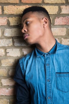 Portrait of handsome dark skinned male model wearing casual clothes against brick wall