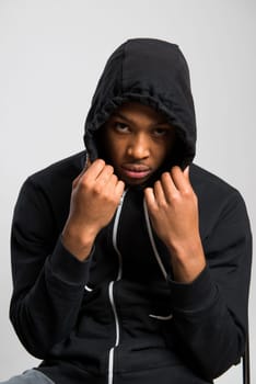 Portrait of suspicious dark skinned male model hiding under black hooded jumper