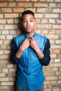 Portrait of handsome dark skinned male model wearing casual clothes against brick wall