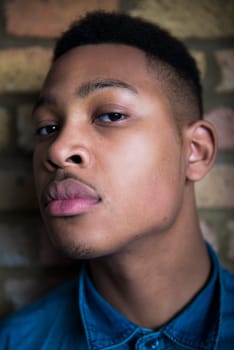 Shallow depth of field portrait of handsome dark skinned male model wearing casual clothes against brick wall