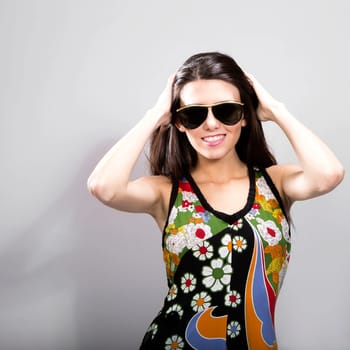 Happy young brunette woman with sun glasses against grey background, Fashion portrait