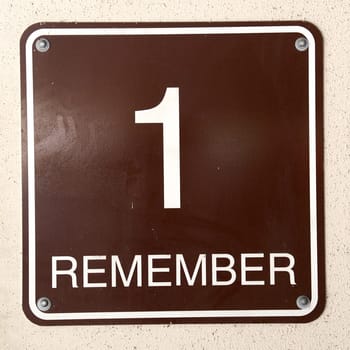 A square sign on wall that states "1 Remember"" as seen near exit of parking garage."