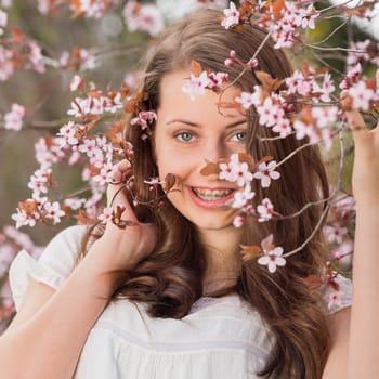 Smiling romantic girl with braces holding blossoming tree branch spring