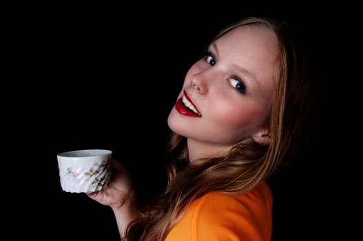 A pretty teenage girl holding a coffee cup and smiling, isolated for.black background..