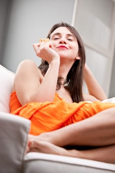 pretty young woman tasting a delicous biscuit in her sofa in complete relax
