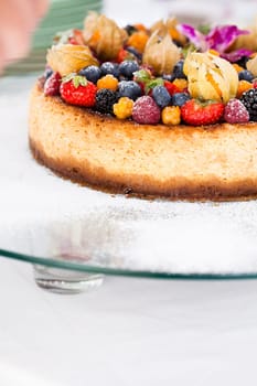 Closeup of delicious sponge cake topped with fresh berries on glass serving tray