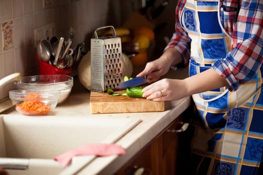 Closeup photo of housewife cutting cucumber with knife