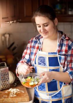 Portrait of young housewife preparing salad with cucumbers