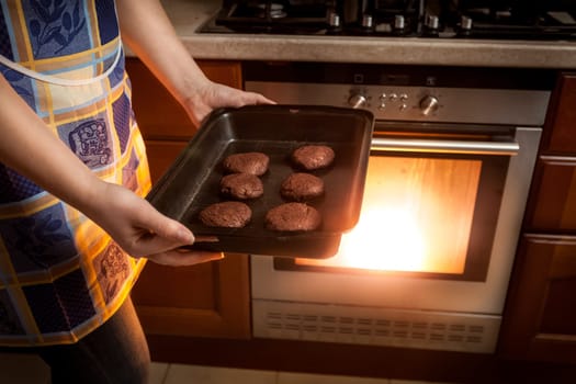 Closeup photo of woman cooking chocolate cookies in hot oven