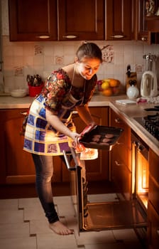 Beautiful woman putting chocolate cookies in hot oven