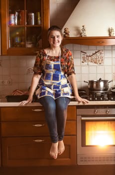 Beautiful smiling woman sitting on tabletop while baking in oven