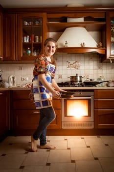 Beautiful housewife baking cookies in oven on country style kitchen