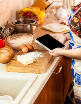 Closeup photo of woman looking recipe on tablet while making dough
