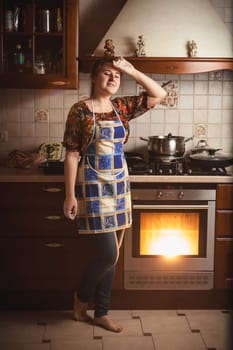Young tired housewife standing near working oven