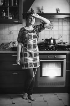 Black and white photo of tired housewife standing on kitchen