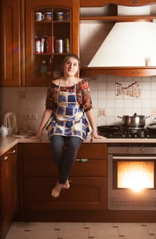Beautiful housewife sitting on tabletop near working oven