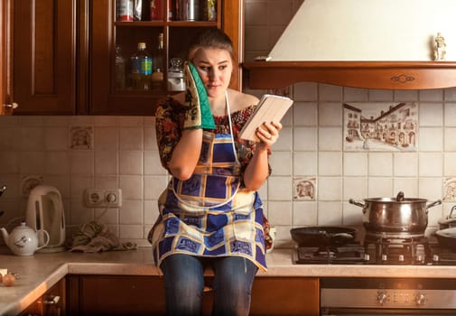Portrait of amazed housewife looking recipe on tablet while sitting on tabletop