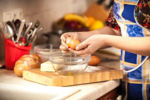 Closeup photo of woman breaking egg in glass bowl