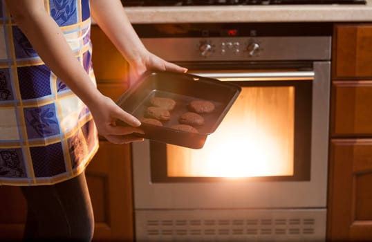 Closeup photo of woman putting cookies in oven
