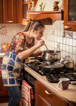 Beautiful woman in apron stirring soup with kitchen spoon
