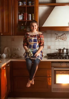 Beautiful woman sitting on tabletop while cooking dinner in oven
