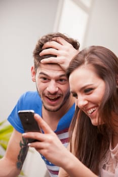 the girl is showing her phone to the boy and they are laughing because they're having fun and they are happy.