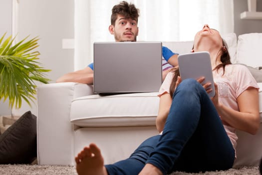 a man and a woman using a notebook and a tablet in their living room