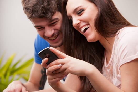 the girl is showing her phone to the boy and they are laughing because they're having fun and they are happy