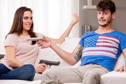 woman on a sofa demanding his boyfriend to give her remote control forcing him with a gun (funny scene)