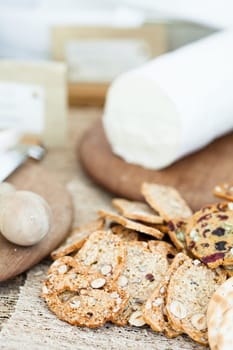 Closeup of dry crackers with cheese on wooden cutting board in background