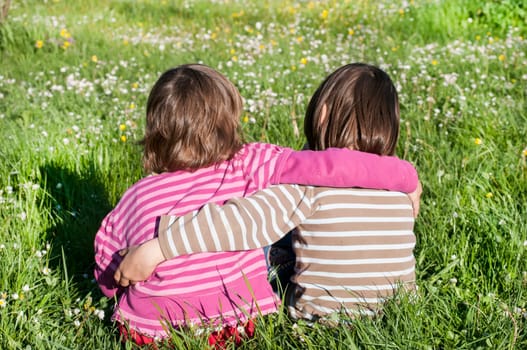 Two children sitting back together on rural meadow