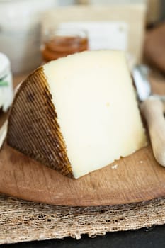 Closeup of piece of cheese on wooden cutting board with condiment in jar in background