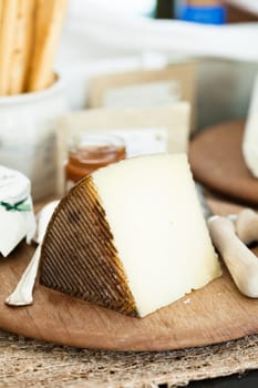 Closeup of piece of cheese on wooden cutting board with condiment in jar in background