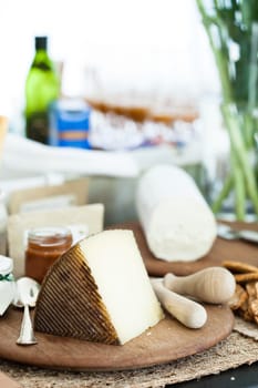 Closeup of piece of cheese and condiment in jar on wooden cutting board with cheese in background