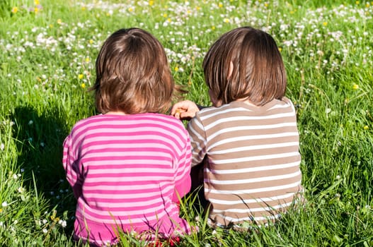 Two children sitting back together on rural meadow